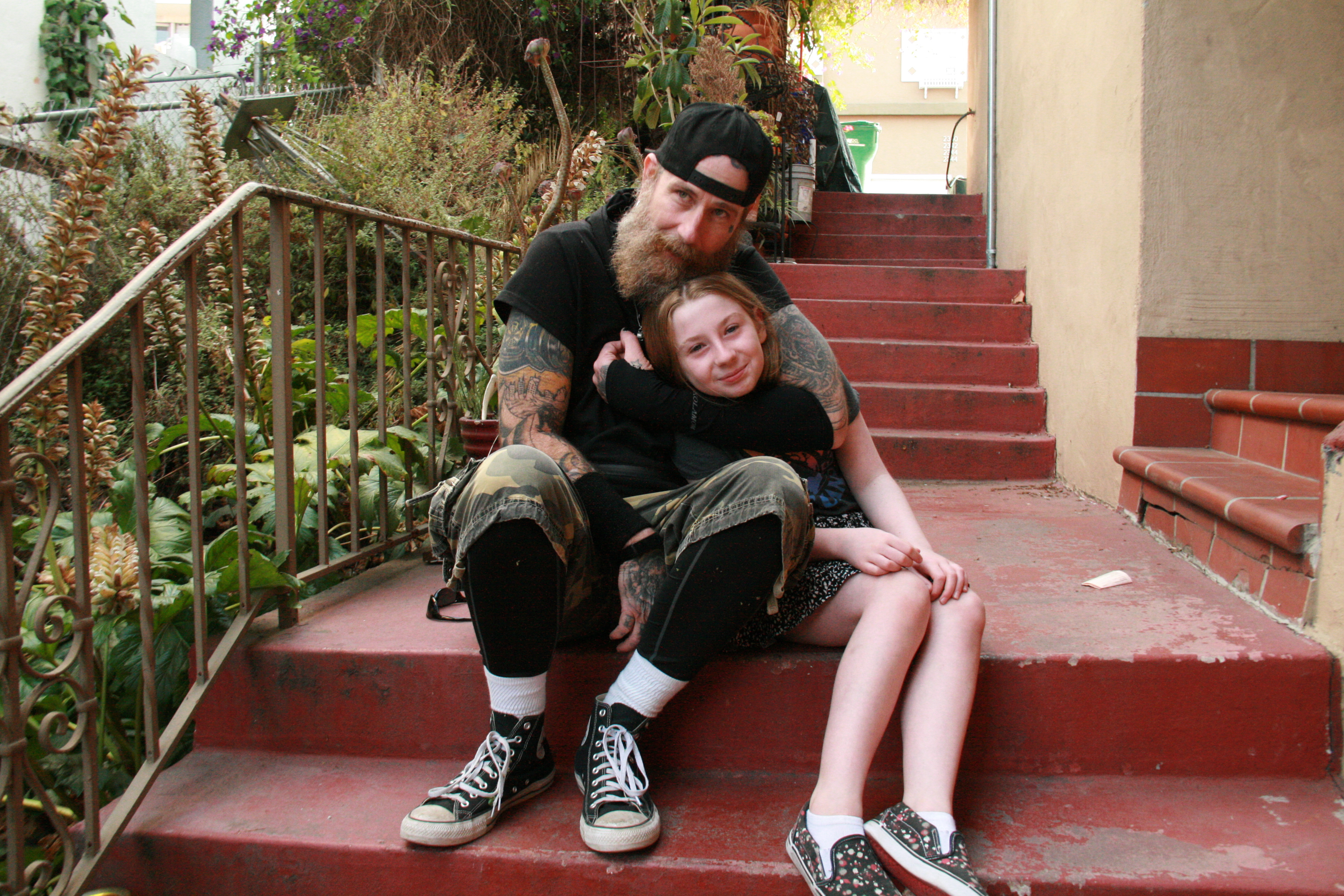 A smiling child (Jett) being hugged by her dad, sitting on some stairs.