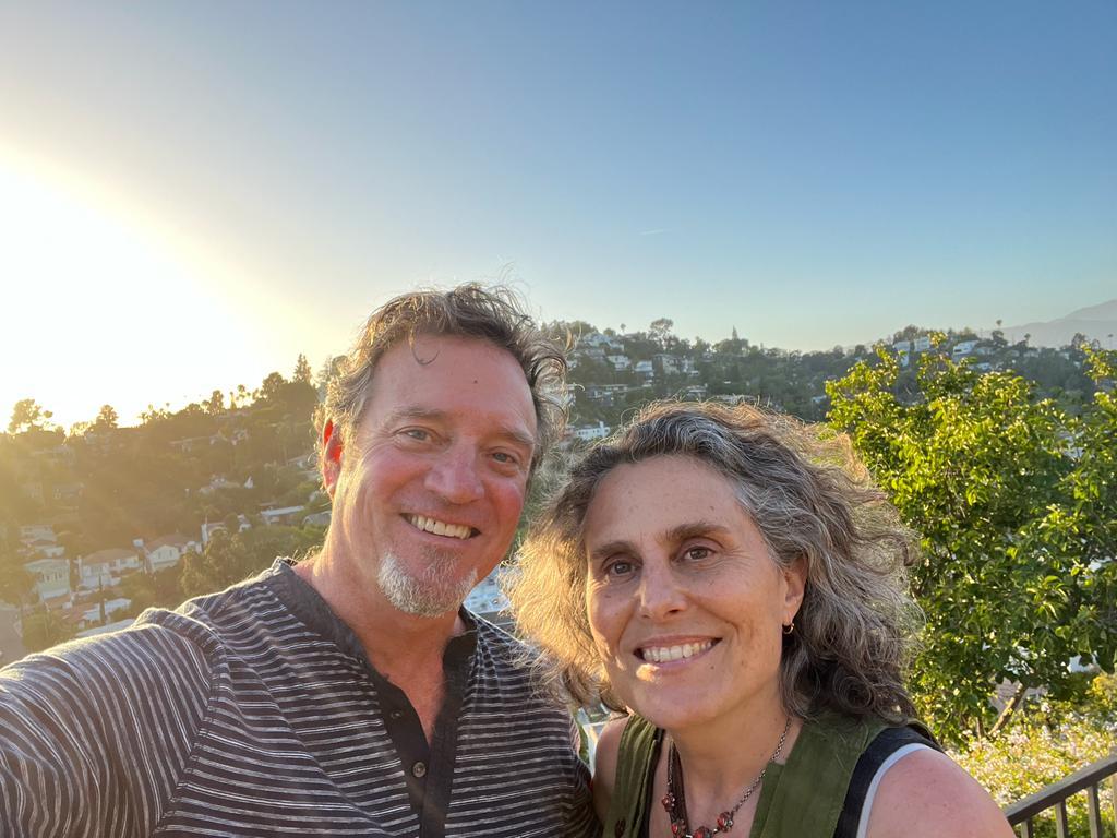 A selfie of Mark (left) and Mara (right) co-founders and publishers of Neighbor2Neighbor, both smiling at the camera with the Los Angeles hills in the background