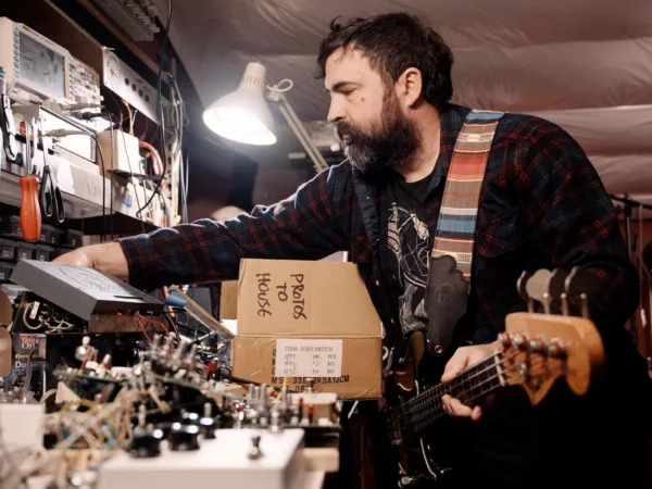 Christopher Benson holds guitar while adjusting amplifier equipment in a studio