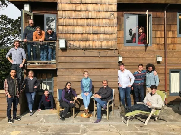 Photo of Momentum's staff from 2019. Some are standing and others are sitting in front of a rustic building.