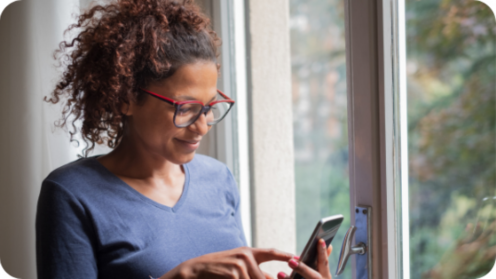 Woman Wearing Glasses Looking At Her Phone And Smiling